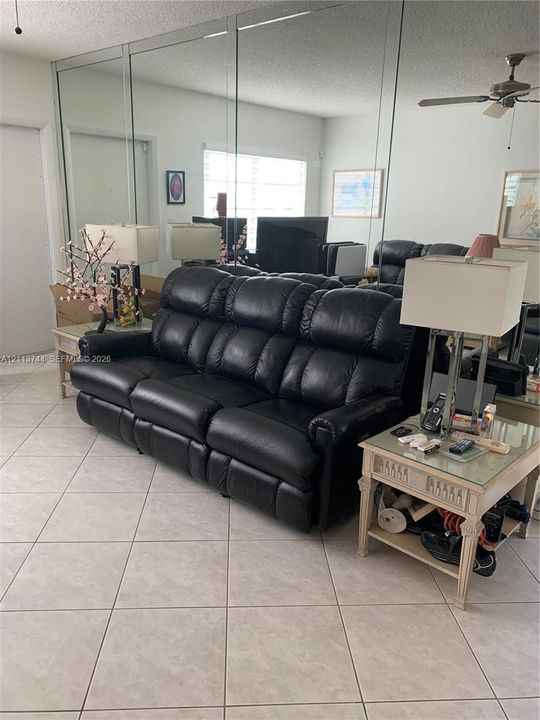 Living area featuring large-format ceramic tile flooring, floor-to-ceiling wall-mounted mirrors, and a ceiling-mounted fan