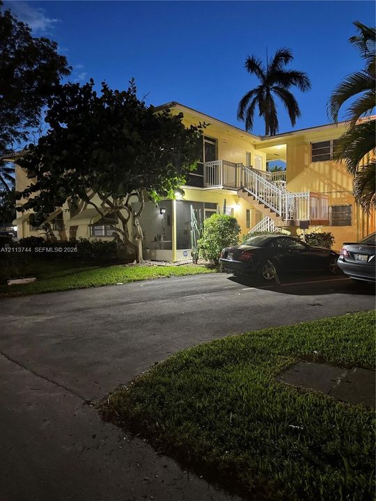 Two-story exterior featuring a screened-in ground-level patio, an elevated balcony with white metal railings, and an asphalt parking area
