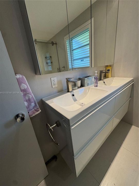 Floating dual-sink vanity featuring a high-gloss finish, integrated basins, and minimalist chrome faucets, complemented by a wide medicine cabinet and large-format floor tiling