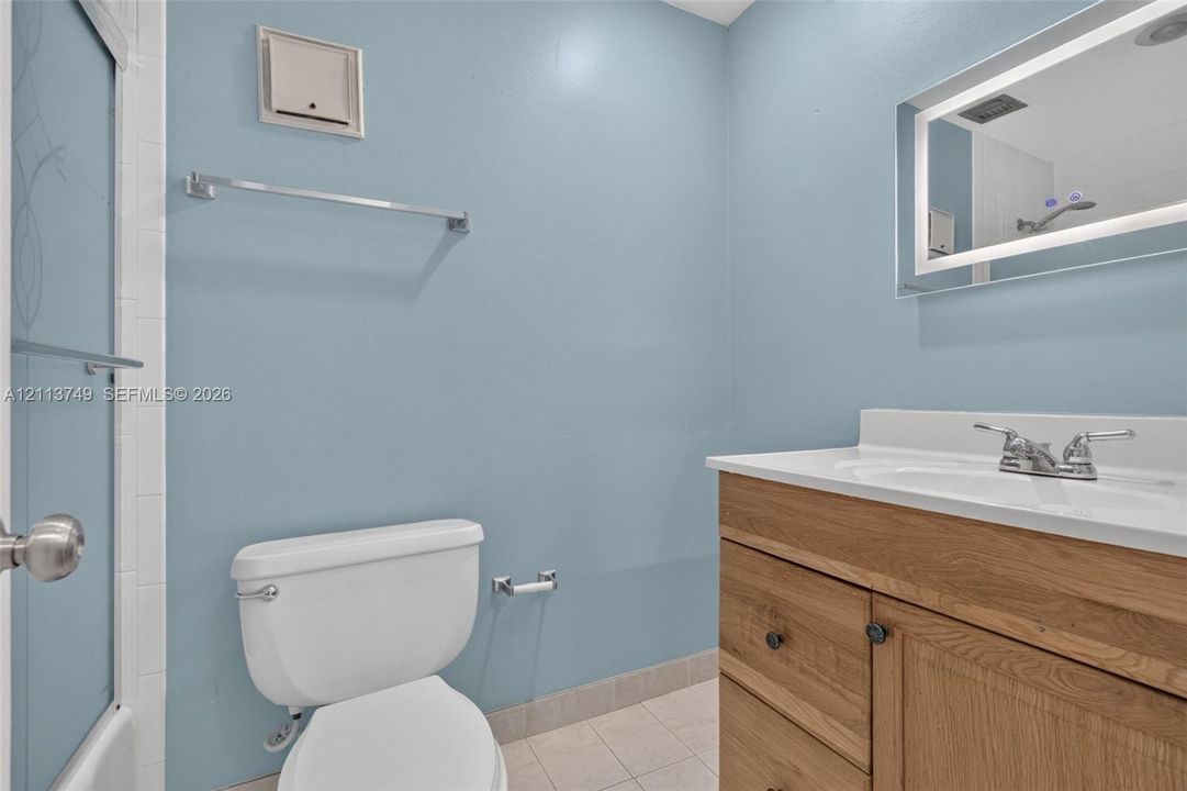 Bathroom featuring a wood-finish vanity with a white countertop, an integrated sink, an illuminated vanity mirror, and a shower with a sliding glass door