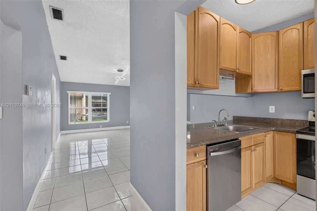 Kitchen featuring wood cabinetry, stone-finish countertops, stainless steel dishwasher, and tile flooring throughout the interior