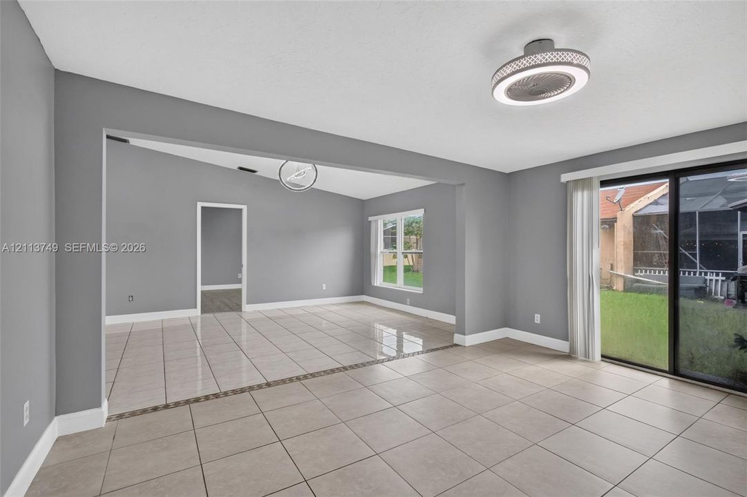 Open-concept interior featuring oversized neutral tile flooring, vaulted ceilings, dual modern LED ceiling fixtures, and sliding glass doors