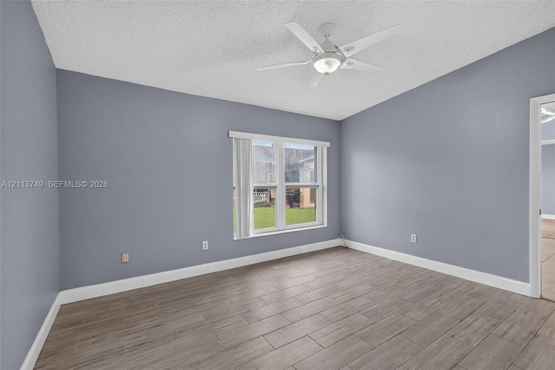 Room featuring wood-finish tile flooring, neutral wall paint, a multi-pane window with vertical blinds, and a central ceiling fan with integrated lighting