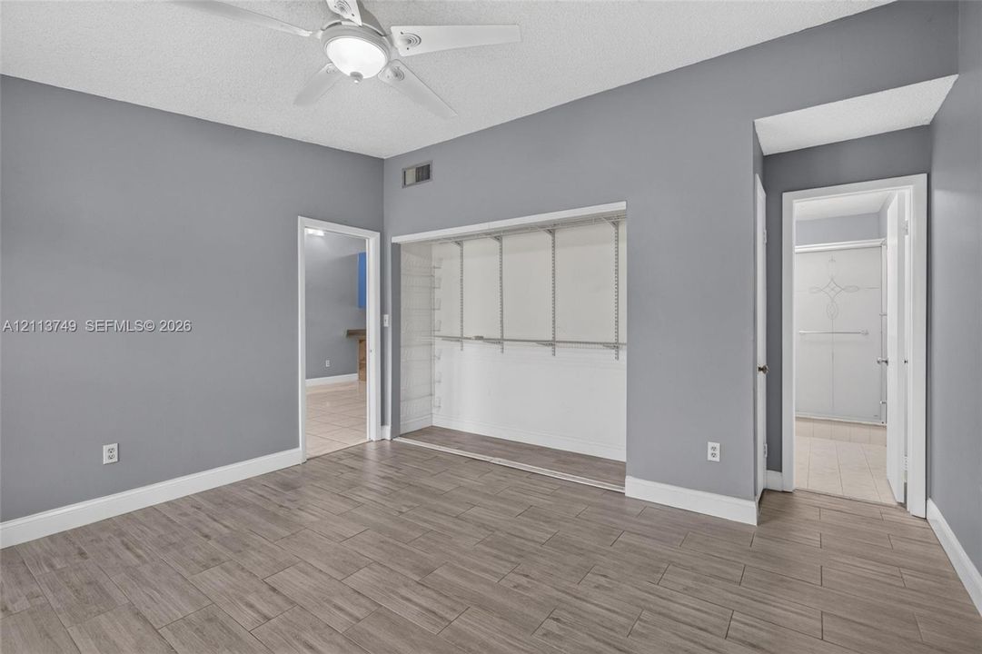 Neutral interior featuring wood-finish tile flooring, ceiling-mounted light fixture with fan, and open-style closet with built-in metal shelving