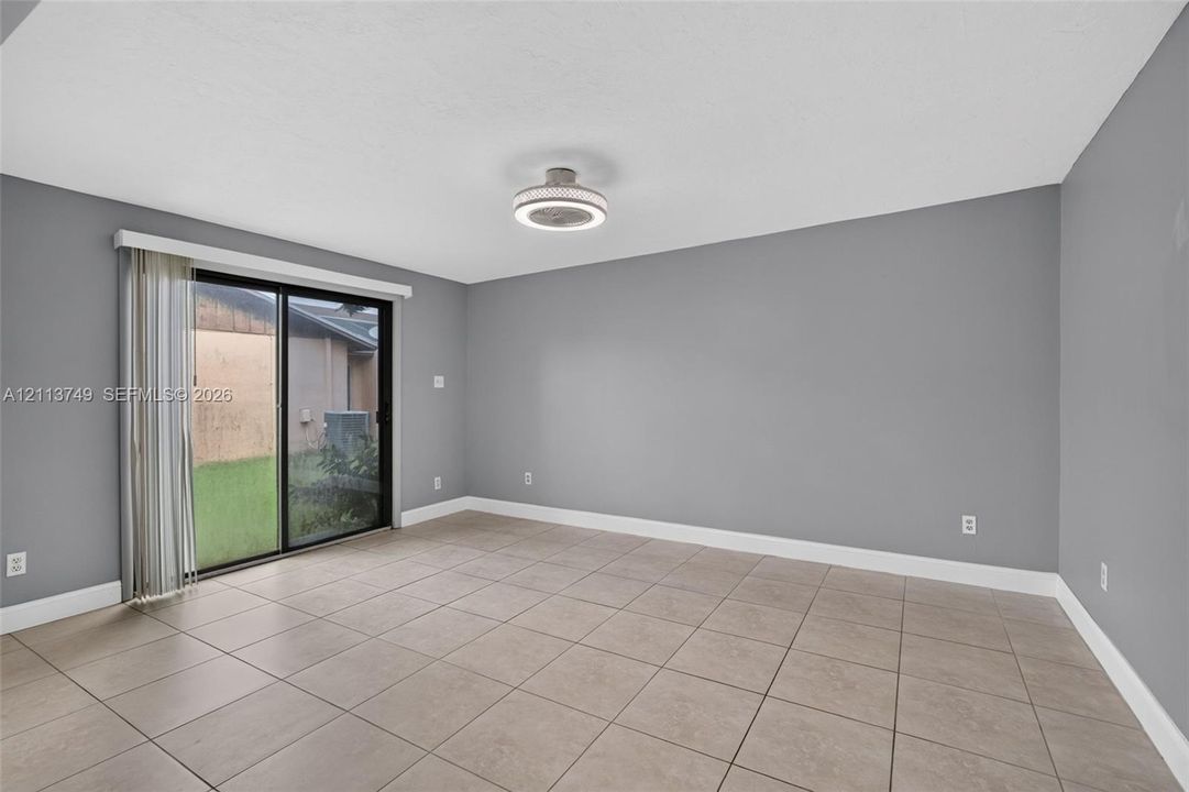 Neutral-toned room featuring large-format ceramic tile flooring, sliding glass door, and a modern circular flush-mount ceiling light