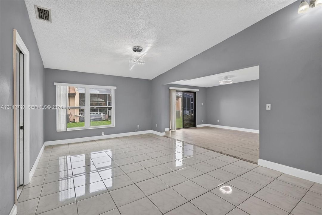 Open-concept interior featuring high ceilings, polished ceramic tile flooring, a multi-pane window, and sliding glass doors