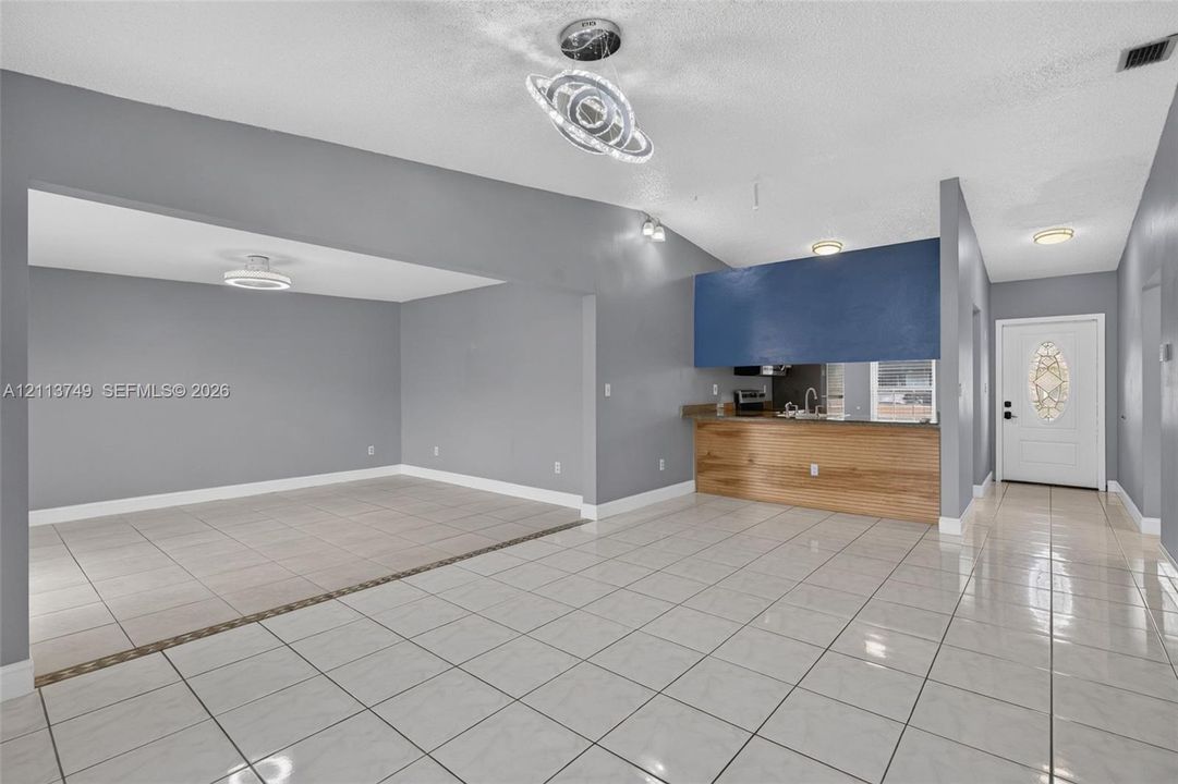 Ceramic tile flooring, vaulted ceilings, modern sculptural chandelier, wood-finish breakfast bar, and exterior door with decorative glass insert