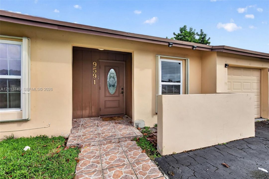 Exterior facade featuring a stucco finish, an entry door with an oval glass insert, a paved walkway with decorative stone-patterned tile, and an attached single-car garage