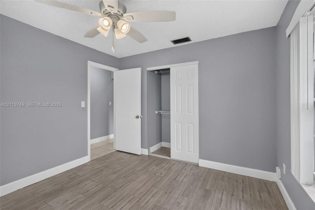 Wood-finish tile flooring, neutral wall paint, multi-light ceiling fan, and sliding closet doors