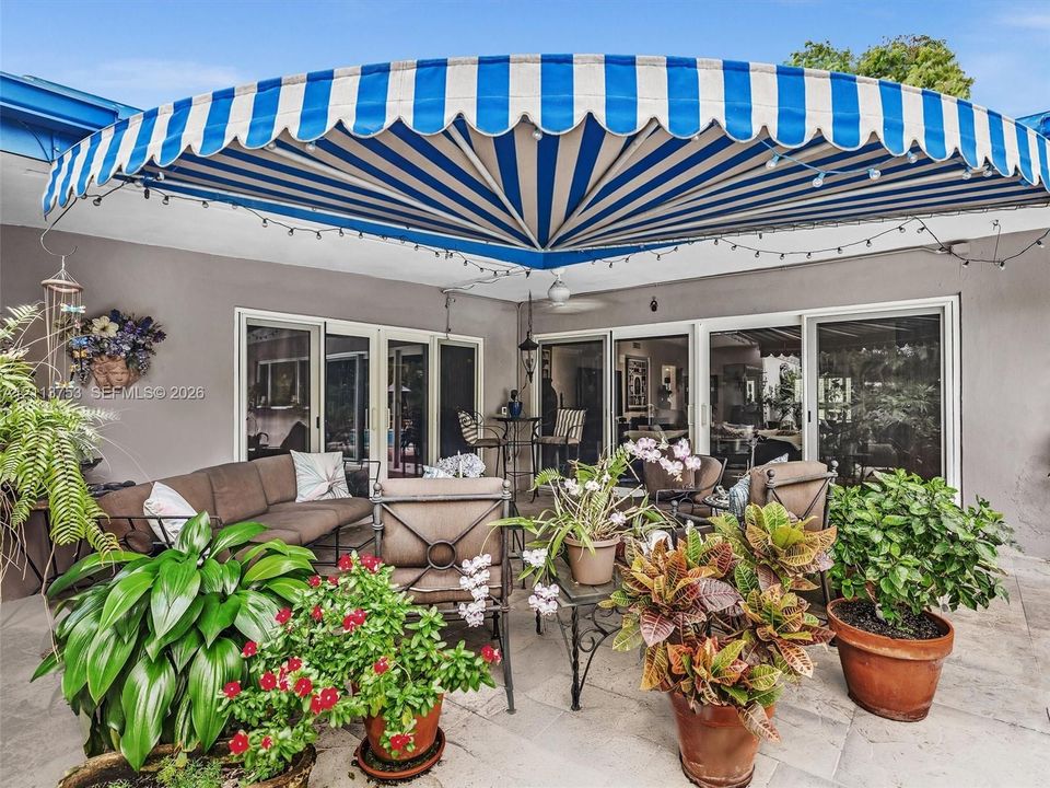 Covered stone-paved patio featuring a retractable blue-and-white striped awning and multiple sliding glass doors