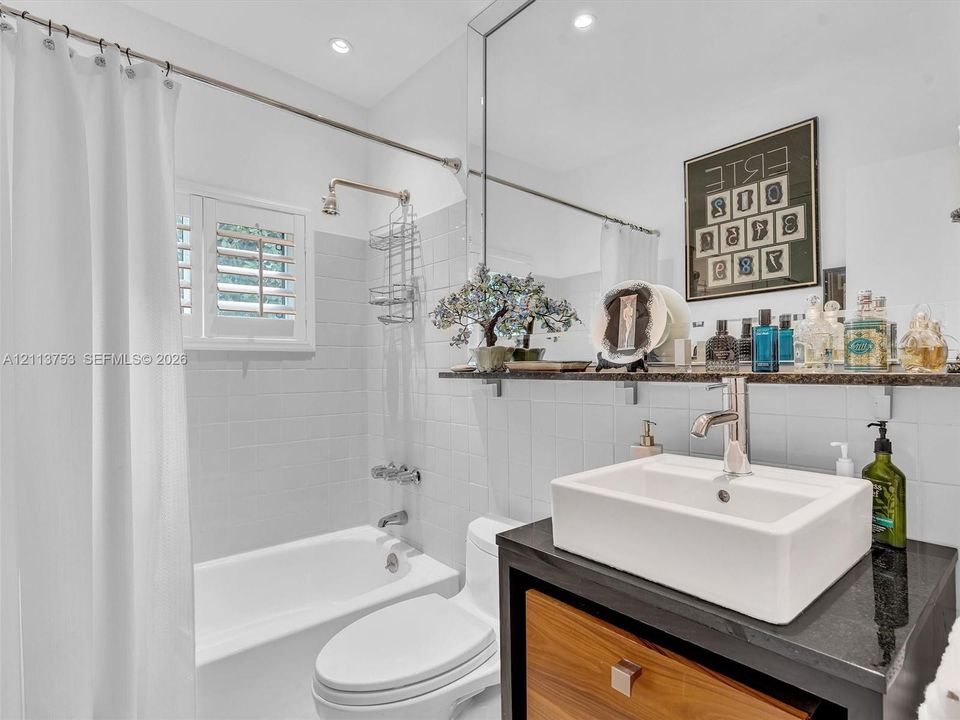 Bathroom featuring a vessel sink with a polished chrome faucet, stone countertop, wood-finish vanity, recessed lighting, and a bathtub with white tile surround