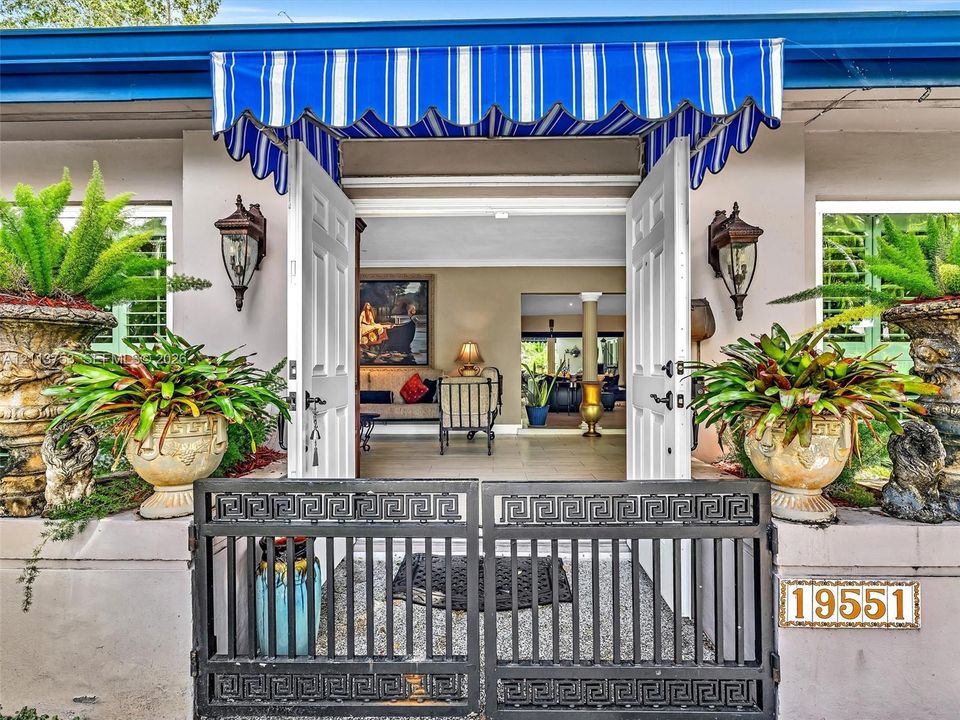 Entryway featuring a striped fabric awning, black metal gate with a Greek key motif, and wall-mounted exterior lanterns