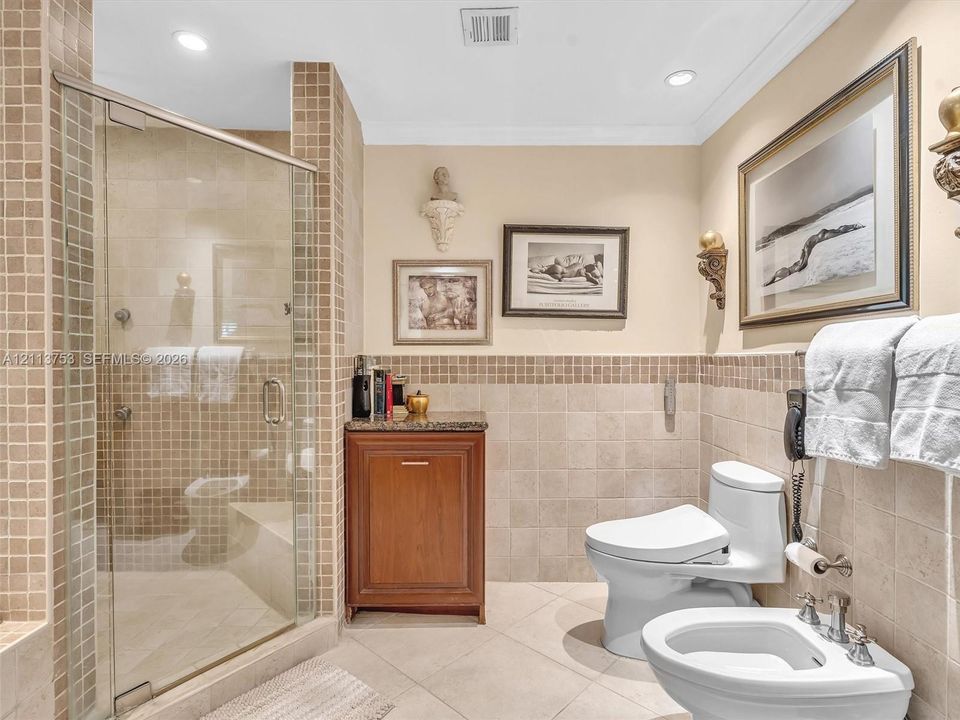 Walk-in shower enclosed in glass with mosaic tile surround, built-in wooden cabinetry with stone countertop, tile flooring, and integrated bidet