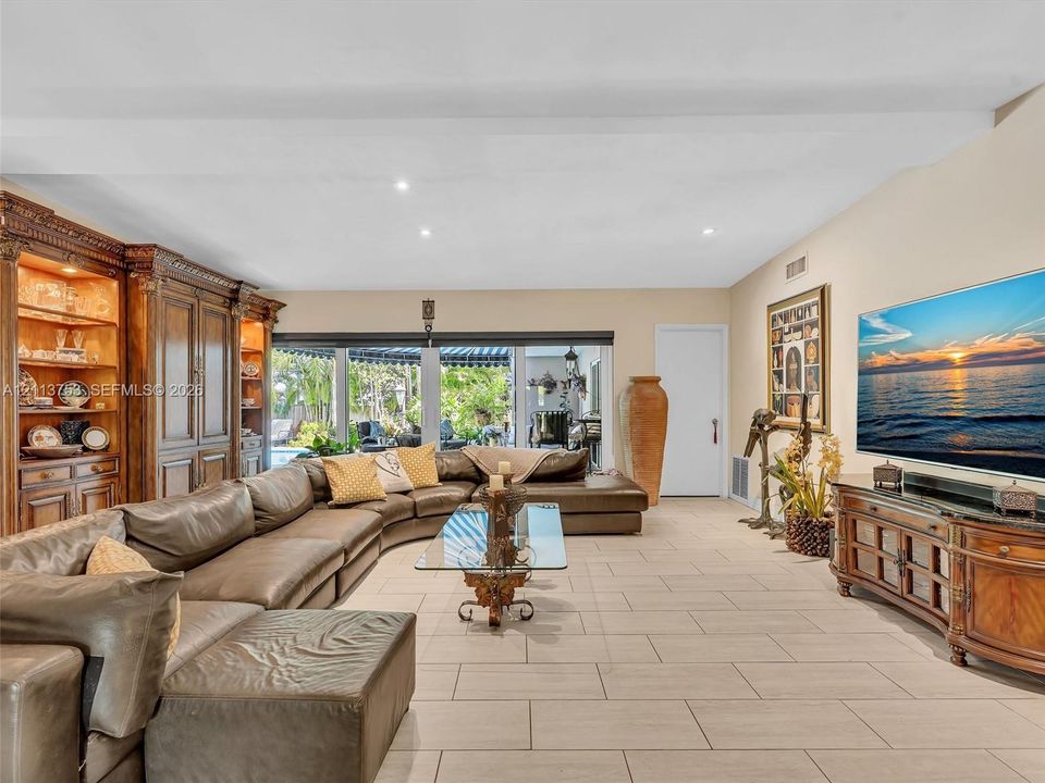 Spacious interior featuring tile flooring, built-in wooden cabinetry, recessed ceiling lighting, a large exterior window opening, and a white interior door