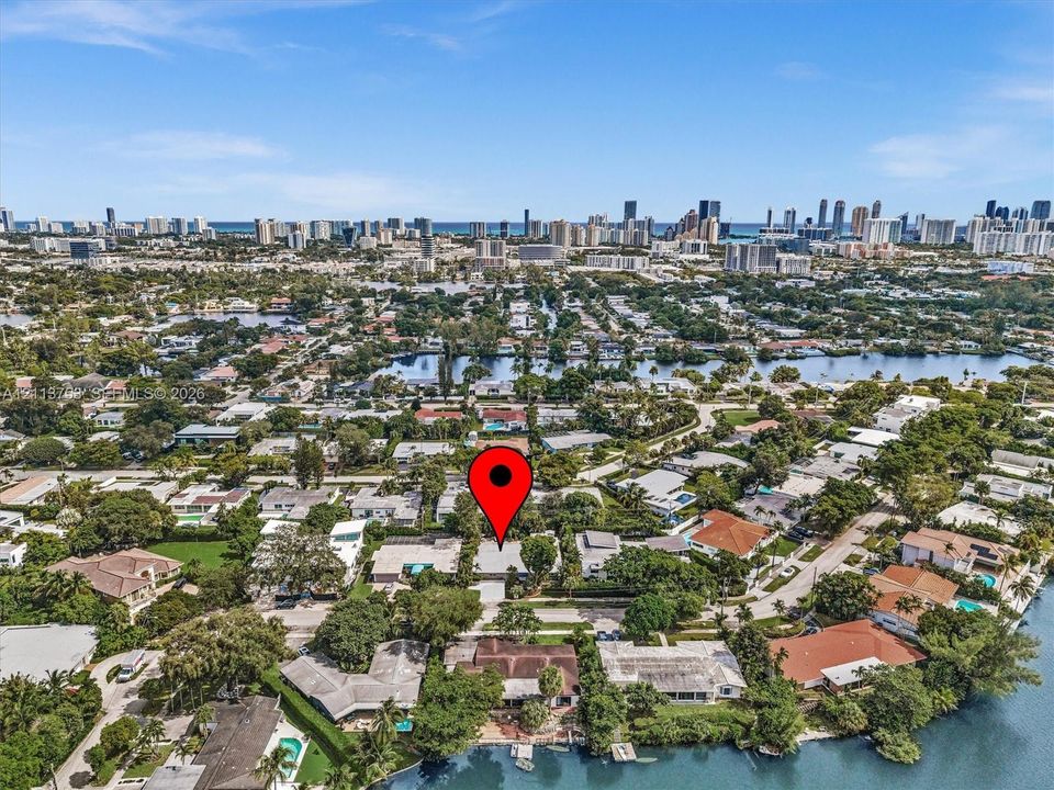 Aerial perspective of a residential property featuring a coastal location with waterway access, mature trees, and proximity to an urban skyline