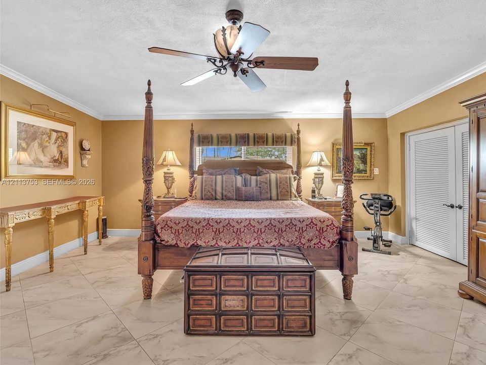 Room featuring large-format tile flooring, crown molding, and a central ceiling fan with integrated light fixture, finished with double louvered doors