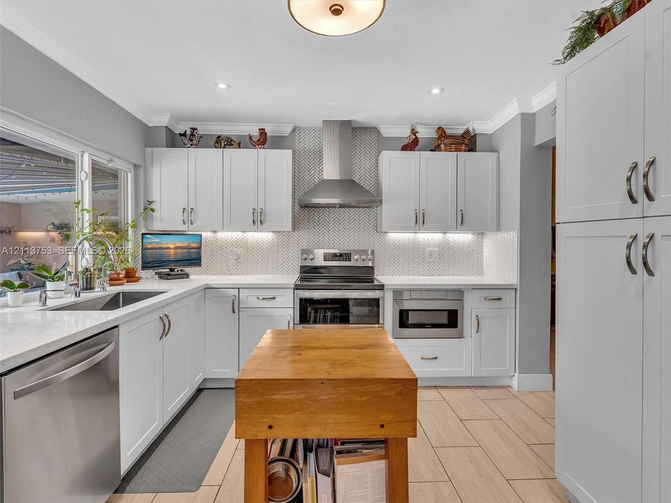 Kitchen featuring white cabinetry, light-colored countertops, stainless steel appliances, herringbone-patterned tile backsplash, and wood-finish tile flooring