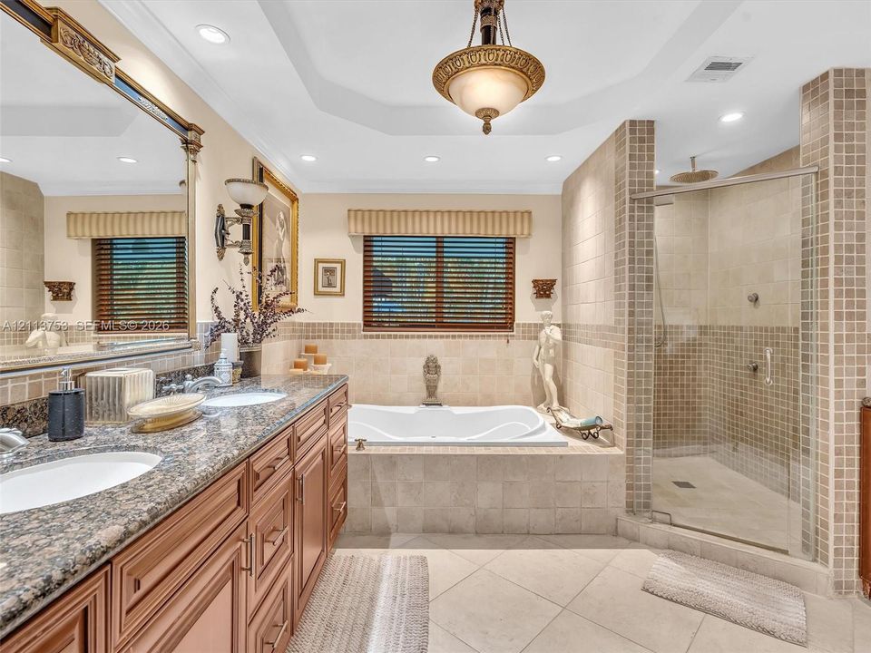 Bathroom featuring a dual-sink vanity with stone countertops, a deep soaking tub, a walk-in glass-enclosed shower with tiled surround, and decorative pendant lighting