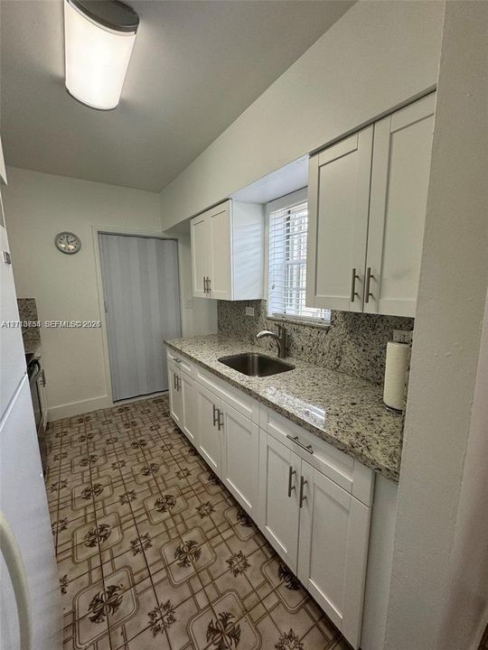 Kitchen featuring white cabinetry with metallic pulls, stone-composite countertops, integrated stainless steel sink, and patterned floor tile