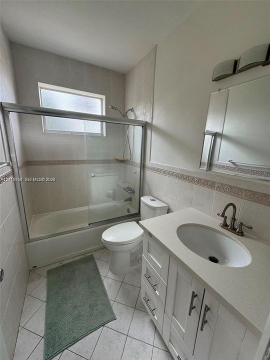 Bathroom featuring a vanity with stone-composite countertop, undermount sink, brushed-metal faucet, tiled shower enclosure with sliding glass door, and tiled flooring