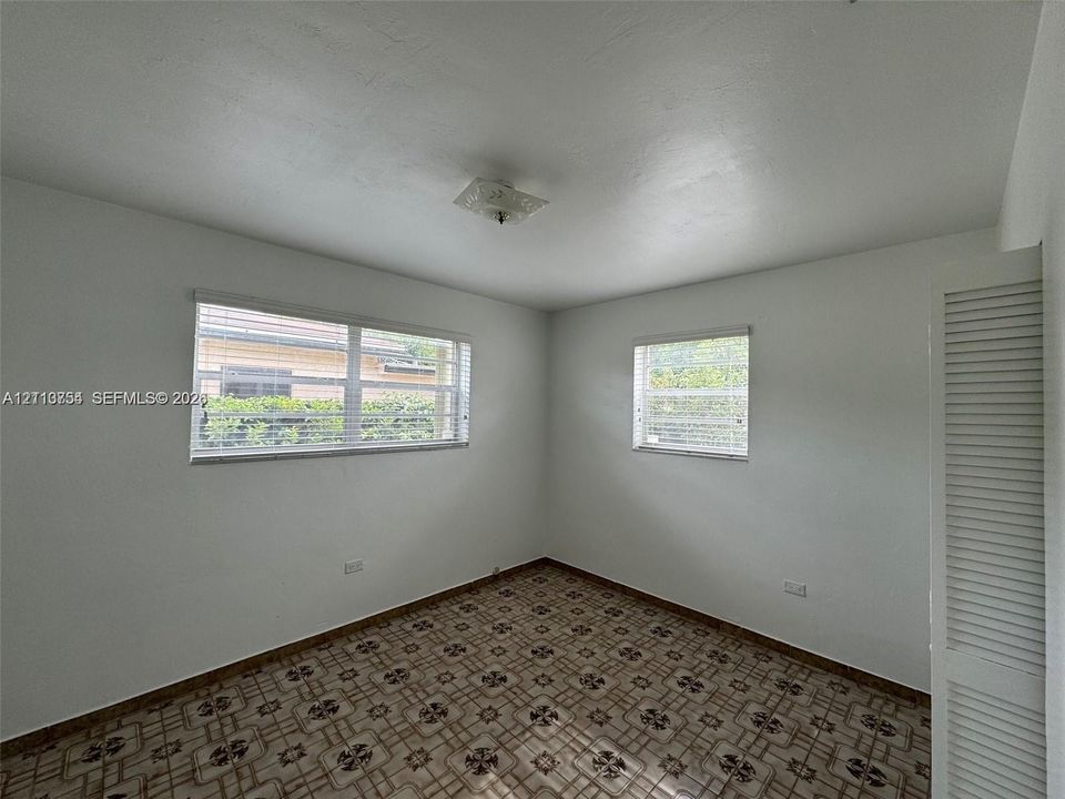 Room featuring patterned tile flooring, two horizontal sliding windows with blinds, a ceiling-mounted light fixture, and a louvered-door closet