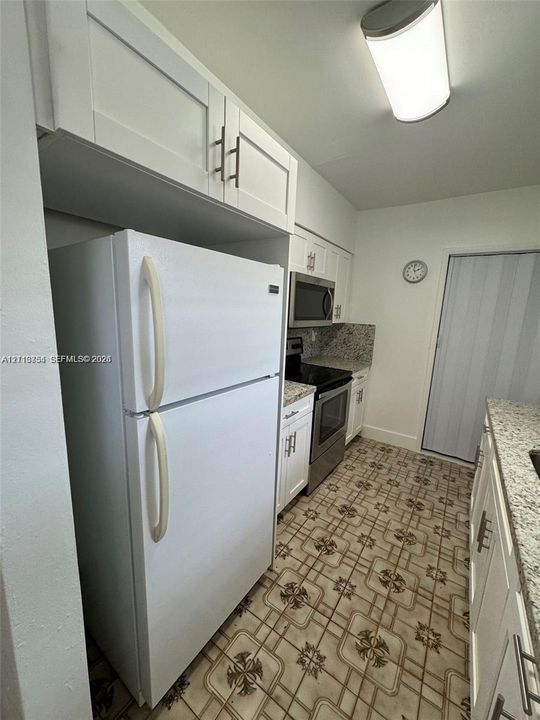 Kitchen featuring white shaker-style cabinetry, stone-finish countertops, stainless steel appliances, and patterned floor tile
