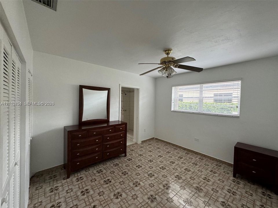 Room featuring patterned ceramic tile flooring, ceiling fan with light fixture, louvered closet doors, and large horizontal window