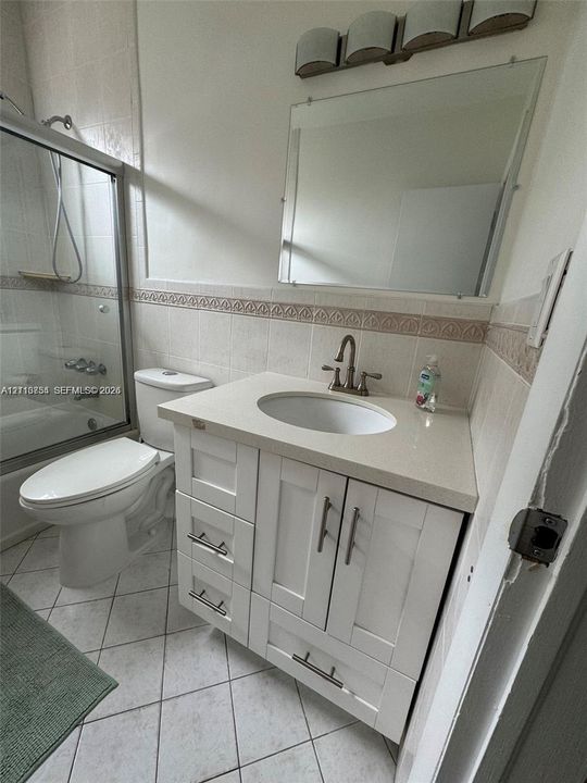 White vanity with stone-composite countertop, undermount sink, brushed-metal hardware, and tiled shower enclosure