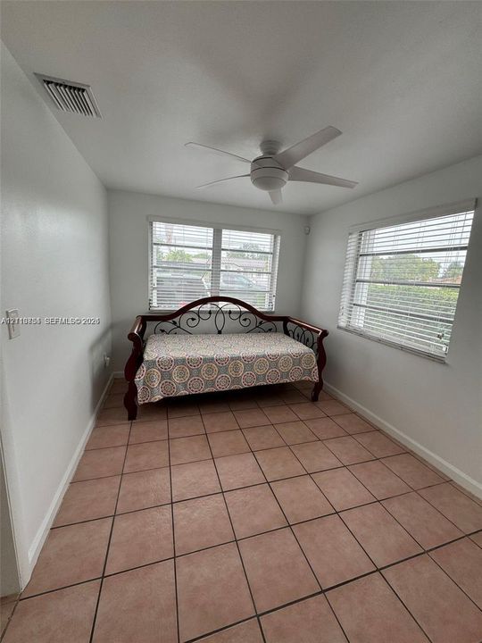 Room featuring tile flooring, a white ceiling fan with integrated lighting, and multiple windows with horizontal blinds
