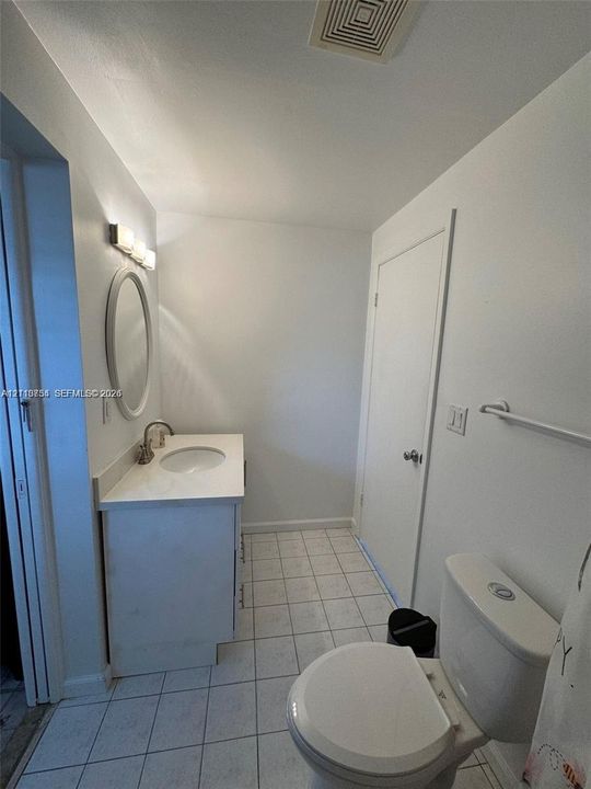 Bathroom featuring a vanity with a white countertop and oval under-mount sink, an oval wall-mounted mirror, four-light vanity fixture, and tiled flooring