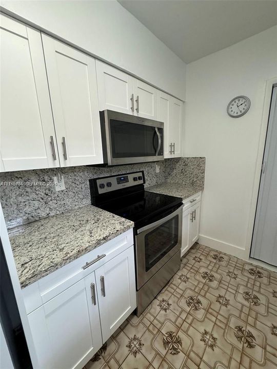 Kitchen featuring white shaker-style cabinetry, stone-finish countertops, and stainless steel appliances including a built-in microwave and range
