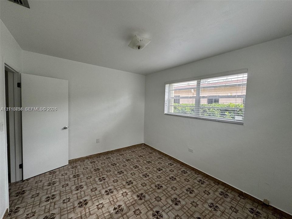 Room featuring patterned tile flooring, a horizontal sliding window with blinds, a flush-mount ceiling fixture, and a white interior door