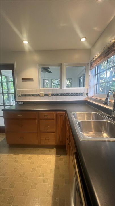 Kitchen featuring wood cabinetry, dark countertops, a double-basin stainless steel sink with a high-arch faucet, patterned tile backsplash, and recessed ceiling lighting