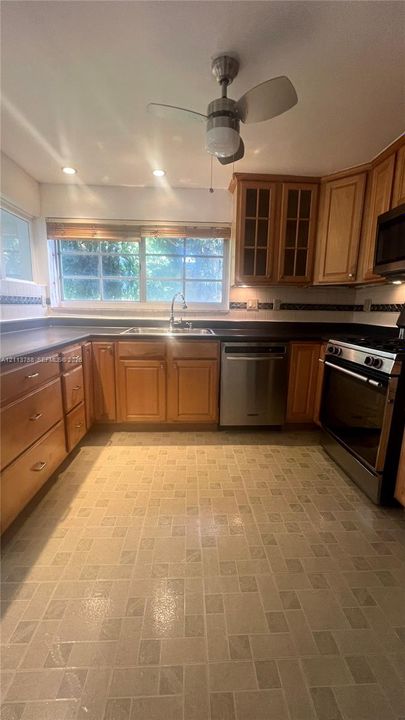 Kitchen featuring wood cabinetry, stainless steel appliances, dark countertops, tiled backsplash, and recessed ceiling lighting