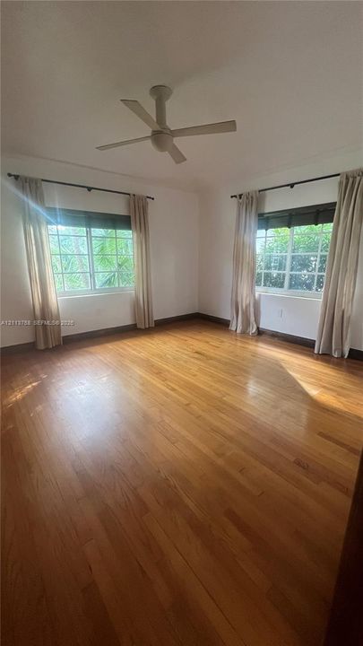 Wood-finish flooring, dual grid-pattern windows, and a ceiling-mounted fan