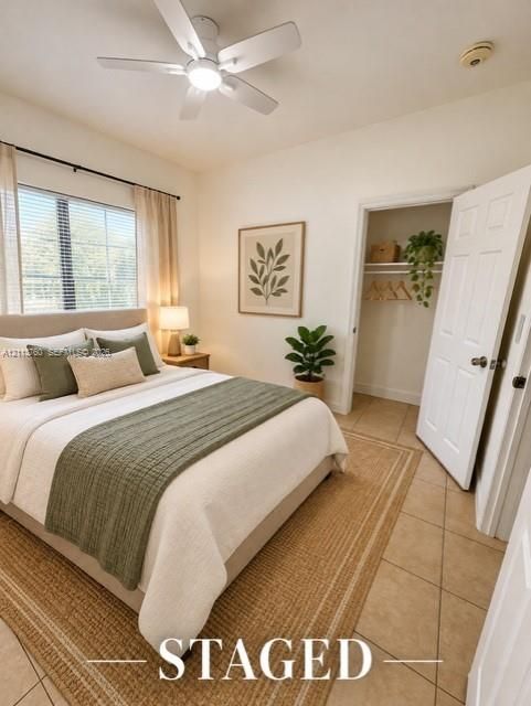 Neutral interior space featuring tile flooring, a multi-blade ceiling fan with integrated lighting, a single-panel interior door, and a built-in reach-in closet with shelving