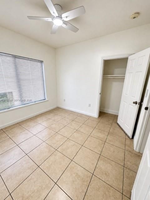 Ceramic tile flooring, white-finish ceiling fan with integrated light, window with horizontal blinds, and closet with built-in shelving
