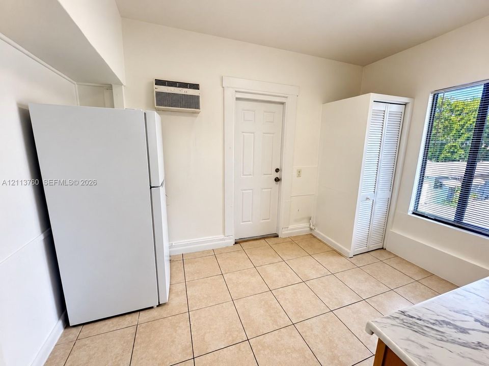 Ceramic tile flooring, white refrigerator, built-in louvered-door cabinet, and wall-mounted air conditioning unit