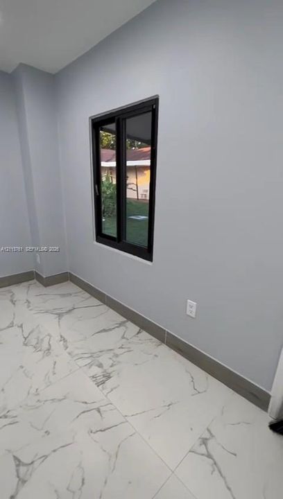 Large-format neutral flooring with veined detailing, light gray interior wall finish, and a black-frame sliding window