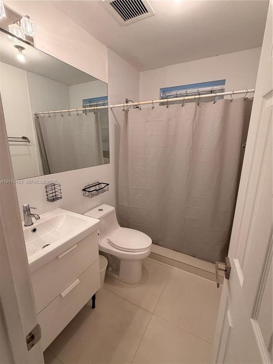 Bathroom featuring a white two-drawer vanity with a porcelain sink, a large frameless wall-mounted mirror, a two-piece toilet, and tile flooring