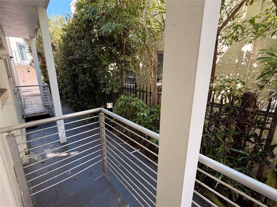 Covered balcony featuring tile flooring, metal horizontal-bar railing, and support columns