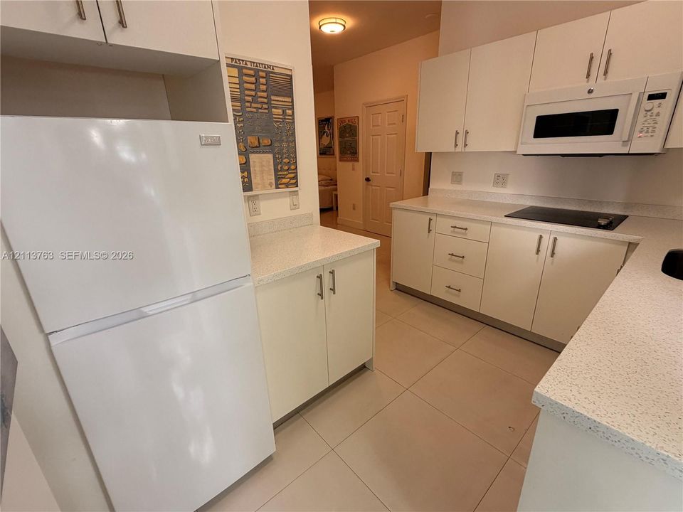 Kitchen featuring white cabinetry, solid-surface countertops, tile flooring, and integrated white appliances including a microwave and refrigerator