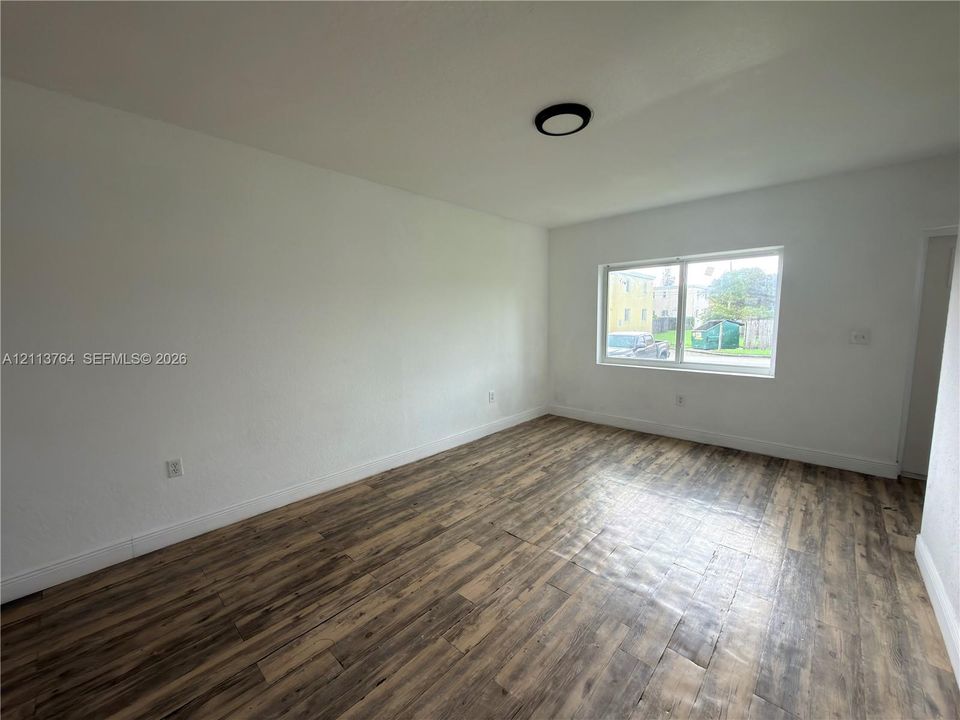 Neutral interior space featuring wood-finish flooring, crisp white walls, and a recessed ceiling light fixture