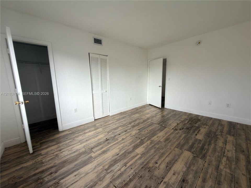 Room featuring wood-finish flooring, white walls, louvered closet doors, and interior hinged doors