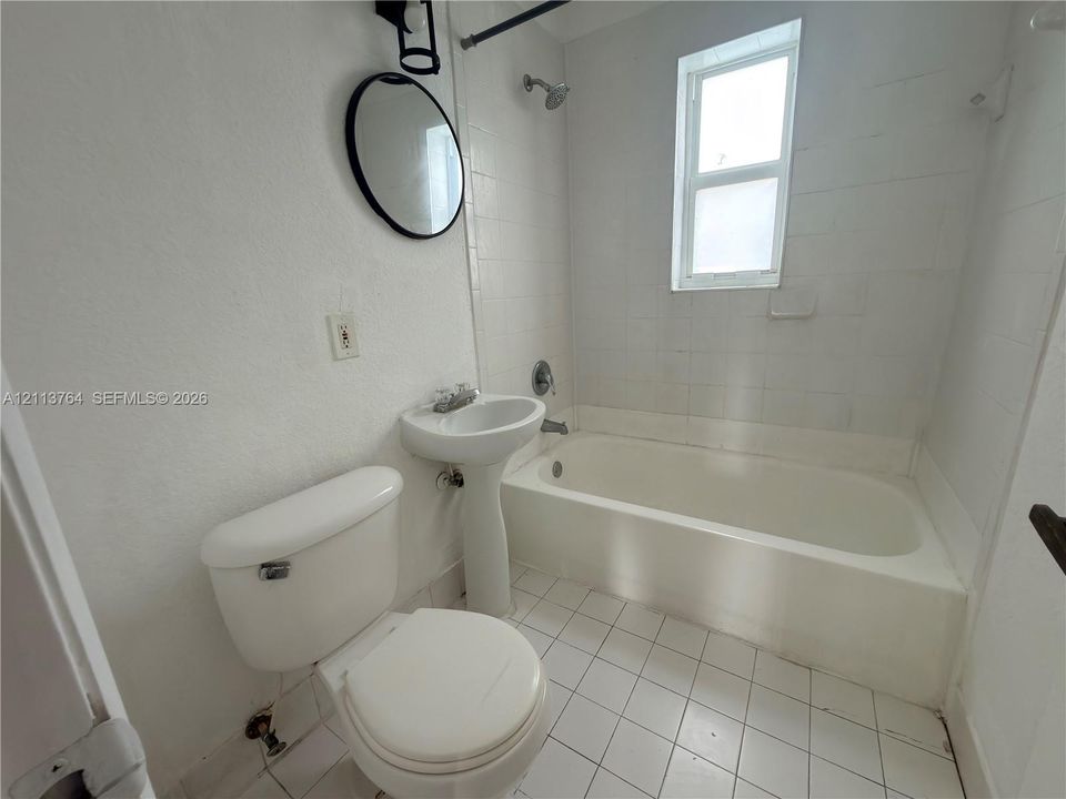 Pedestal sink, tiled shower-tub combination, white ceramic floor tiling, and wall-mounted circular mirror