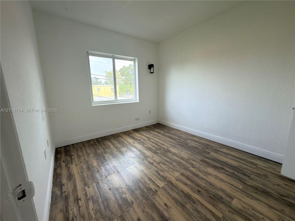 Interior space featuring wood-finish flooring, white walls, a single-hung window, and a wall-mounted light fixture