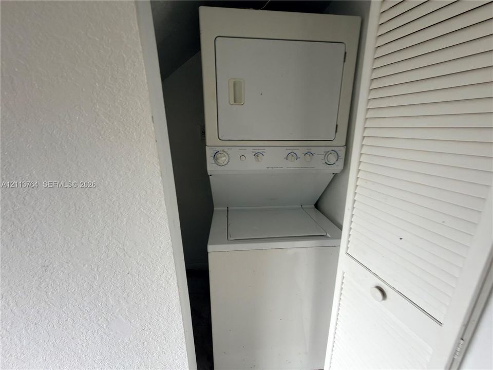 Stackable white laundry unit housed in a recessed closet featuring white louvered doors