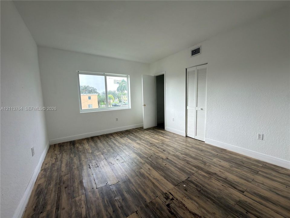 Interior room featuring wood-finish flooring, a single-pane window, and a white louvered bifold closet door