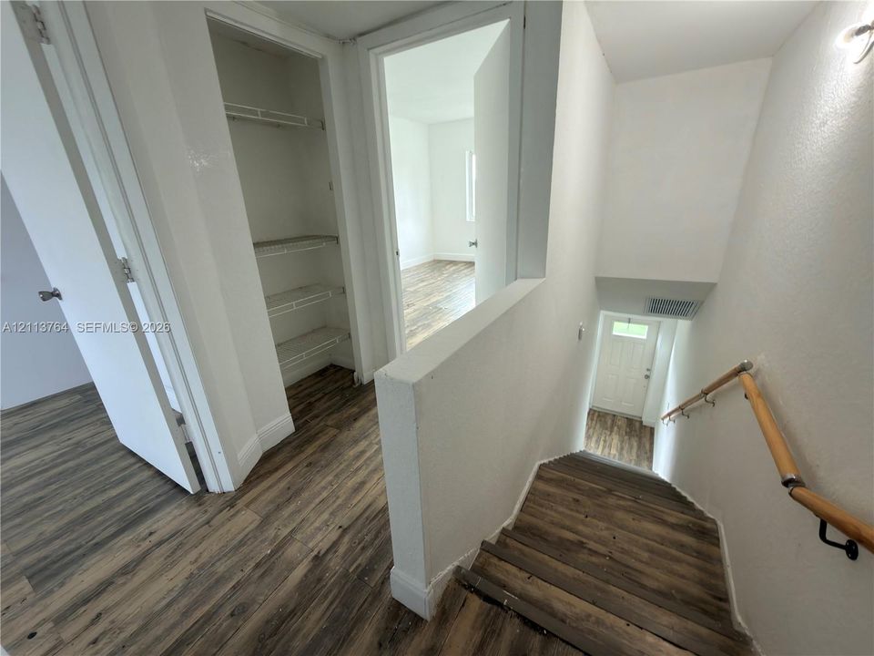 Wood-finish flooring, staircase with a wood handrail, and built-in closet shelving