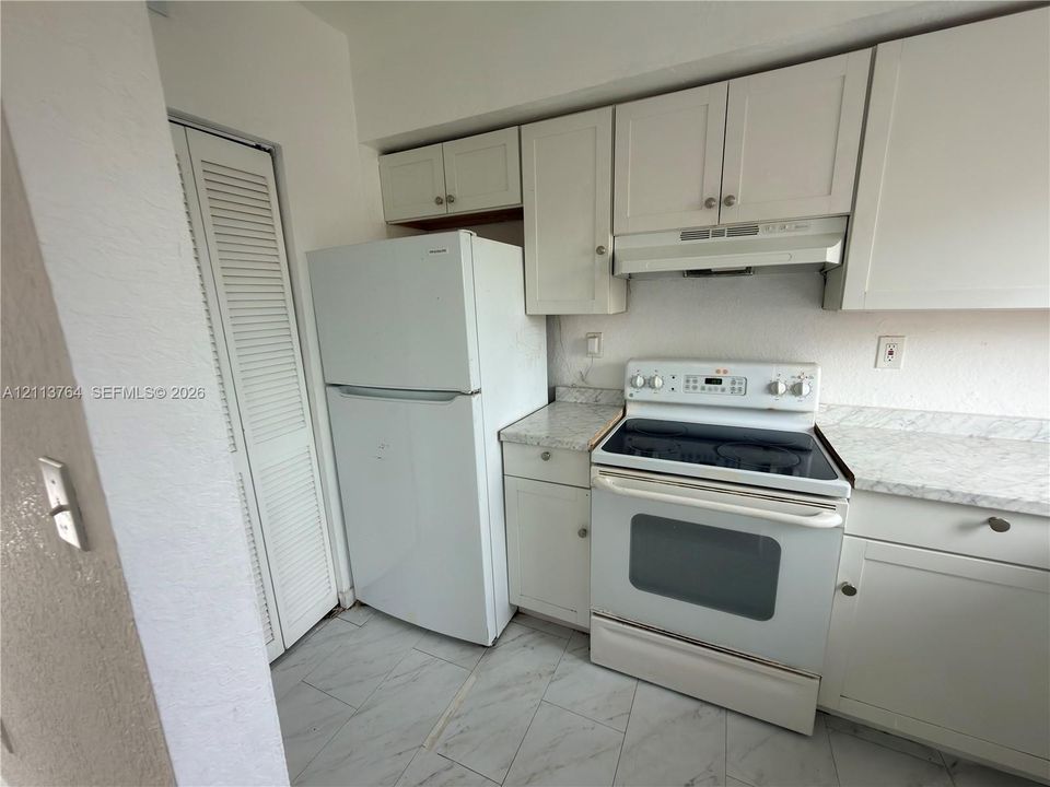 Kitchen featuring white shaker-style cabinetry, stone-patterned laminate countertops, a freestanding electric range, and diagonally laid tile flooring with a louvered-door utility closet